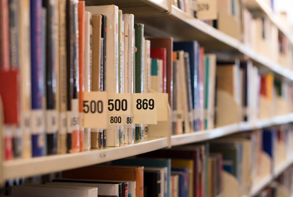 Livros organizados em prateleiras com etiquetas numéricas do sistema CDD